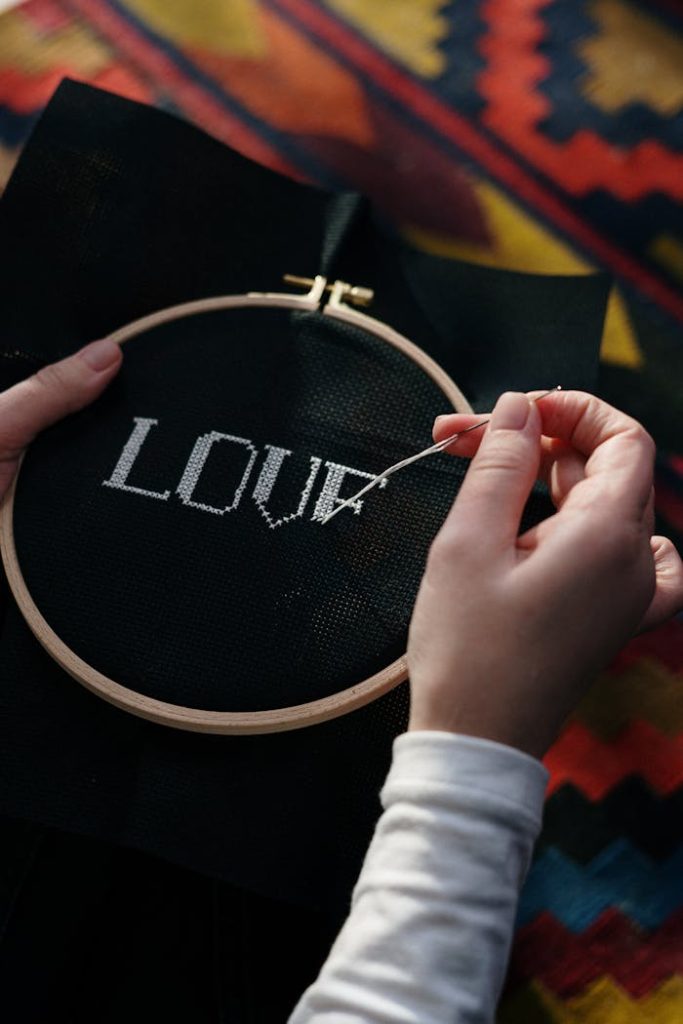 Home Close-up of hands embroidering LOVE onto black fabric using a wooden hoop.