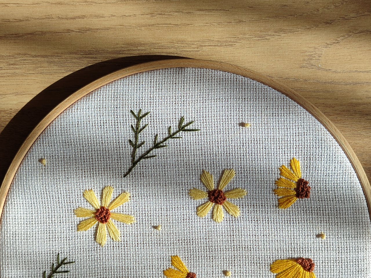 Beautiful embroidery of yellow flowers on canvas, framed in a wooden hoop with natural light.